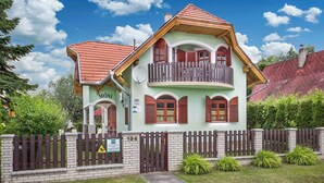 Une maison à deux étages avec un balcon, un toit recouvert de tuiles rouges et une clôture en briques.