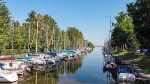 Un port de plaisance où des bateaux sont amarrés le long d’un cours d’eau paisible, entouré d’arbres et d’une zone herbeuse.