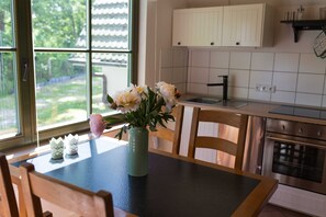A kitchen with a dining table, chairs, a vase with flowers, and a window with a view of greenery.