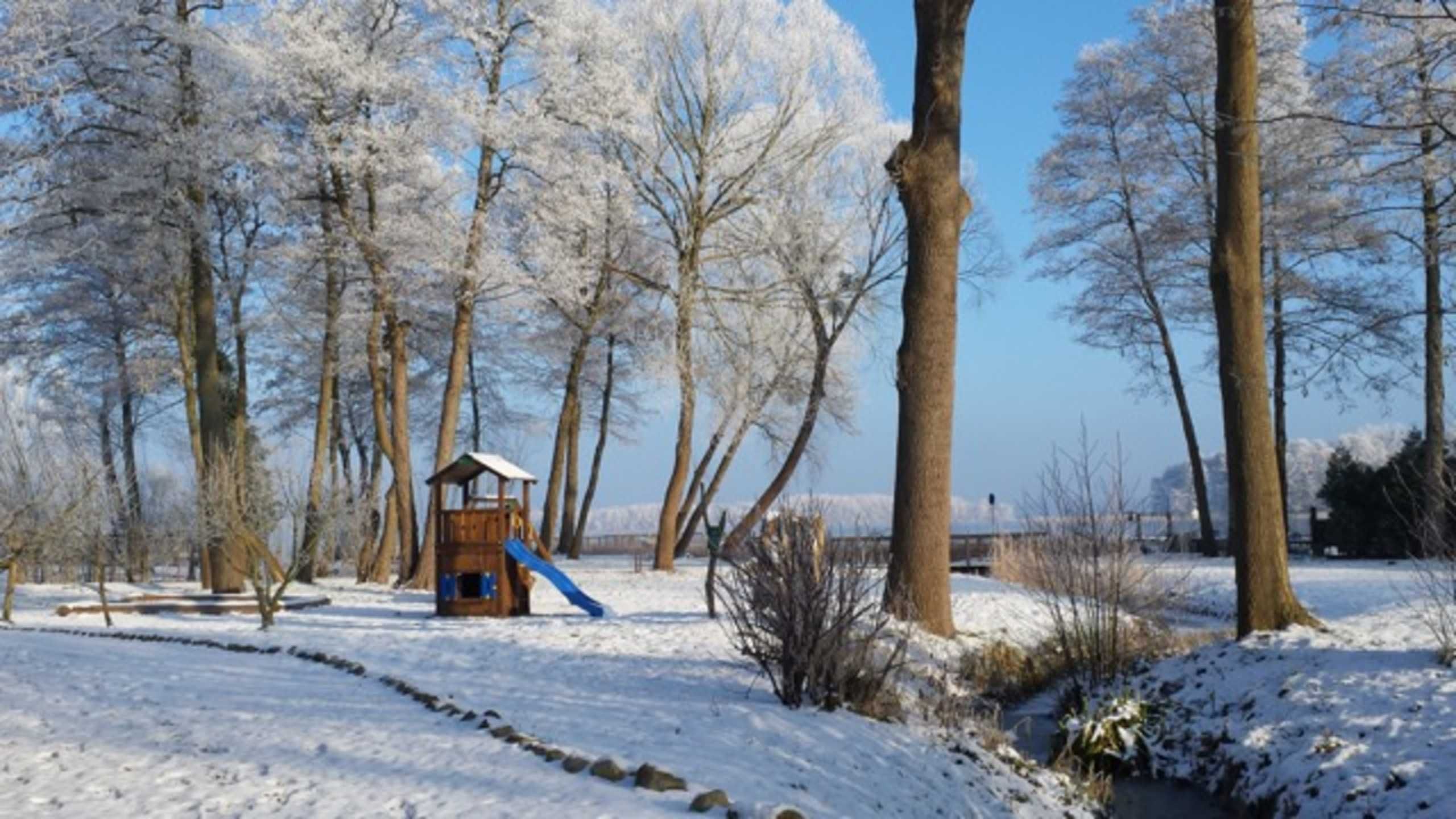A snowy park with a wooden play structure and a slide.
