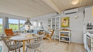 Eine moderne Küche mit weißen Schränken, ein Essbereich mit rundem Tisch und Stühlen sowie Blick auf Grünflächen.