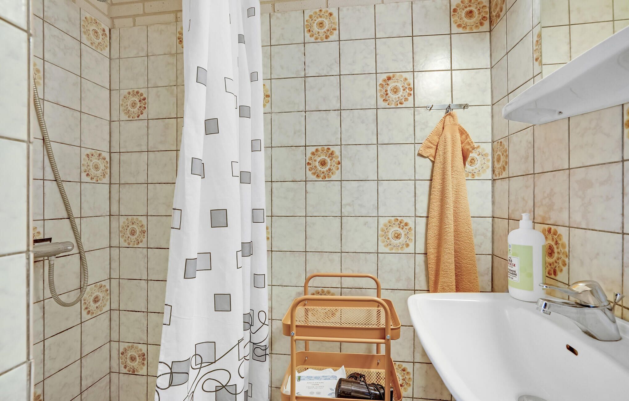 A bathroom with a shower curtain, a towel rack, a sink, and toiletries.