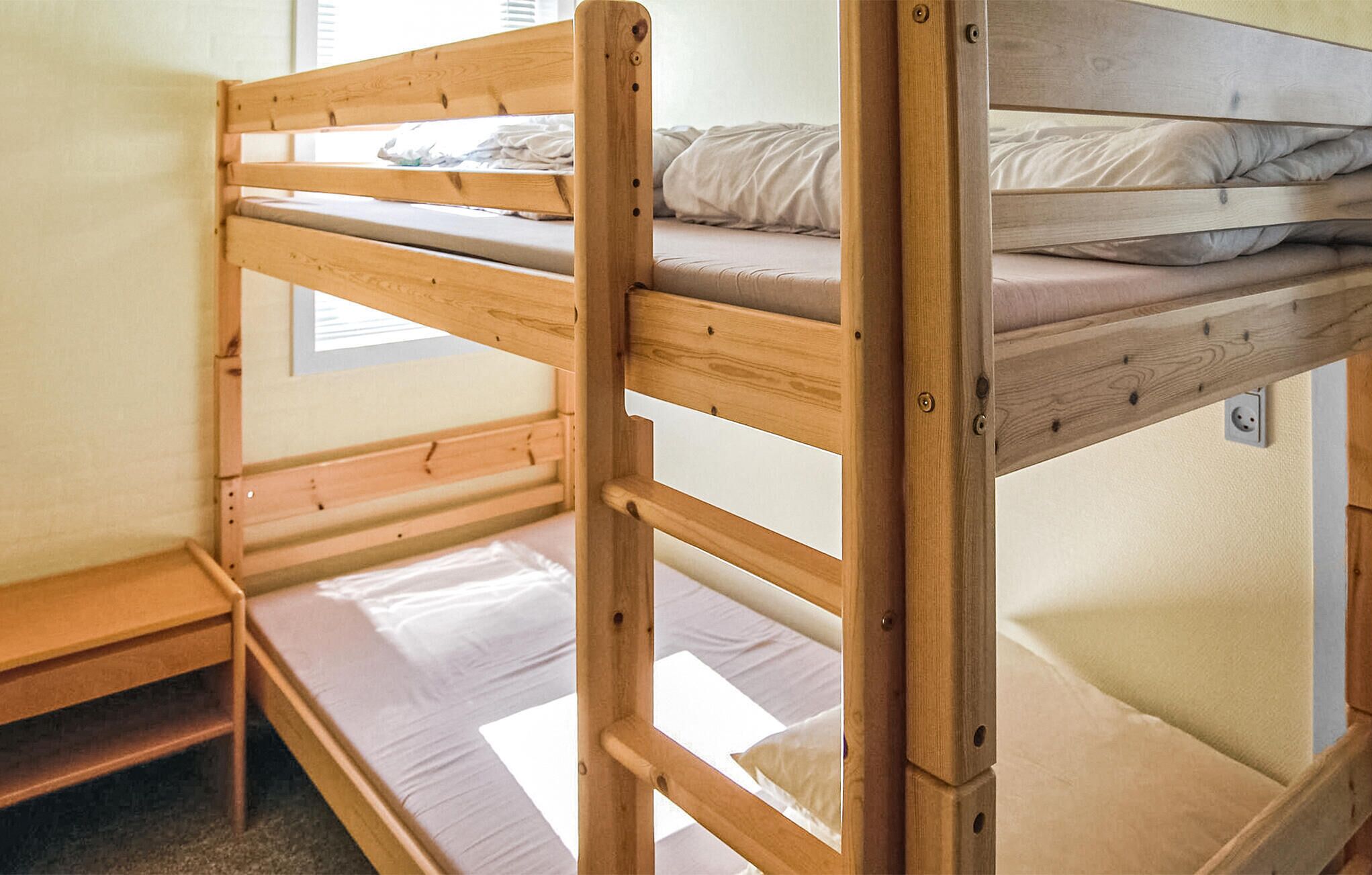 A bunk bed with a wooden frame and a small bench at the foot.