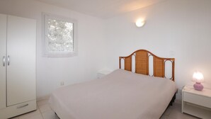 Una camera da letto con un letto, un armadio, un comodino, una lampada e una finestra con tende in pizzo.