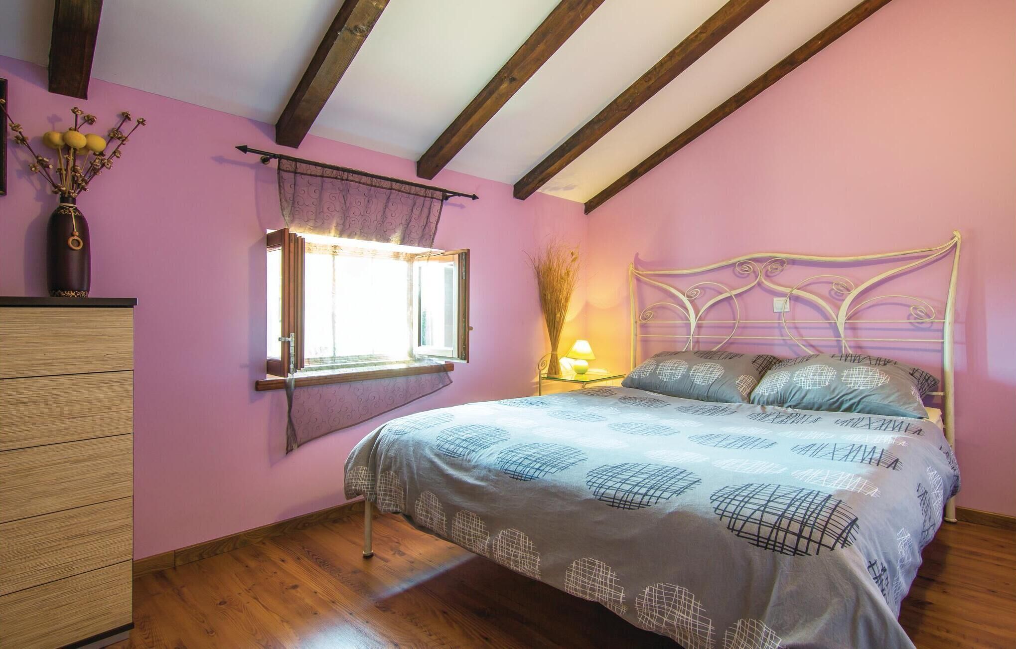 A bedroom with a bed, wooden dresser, window with curtains, and a nightstand with a lamp.