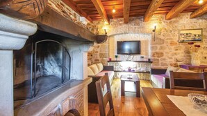 A cozy living room with a stone fireplace, wooden furniture, a flat-screen TV mounted on a stone wall, and a painting above the fireplace. - Awesome home in Porec (Porec)