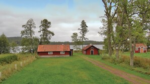 Un paysage rural avec deux maisons en bois rouges, un champ herbeux et un lac en arrière-plan.