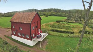 Une grange rouge dotée d’un balcon, entourée de champs verdoyants et d’arbres.