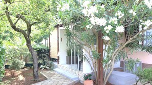 Un jardín con un pórtico, plantas en macetas y un sendero que lleva a un edificio.