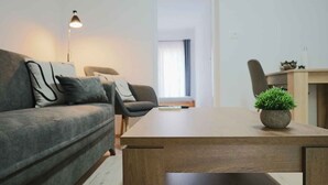 Una sala de estar moderna con un sofá gris, una mesa de centro de madera, una pequeña planta en maceta y un escritorio con una silla.