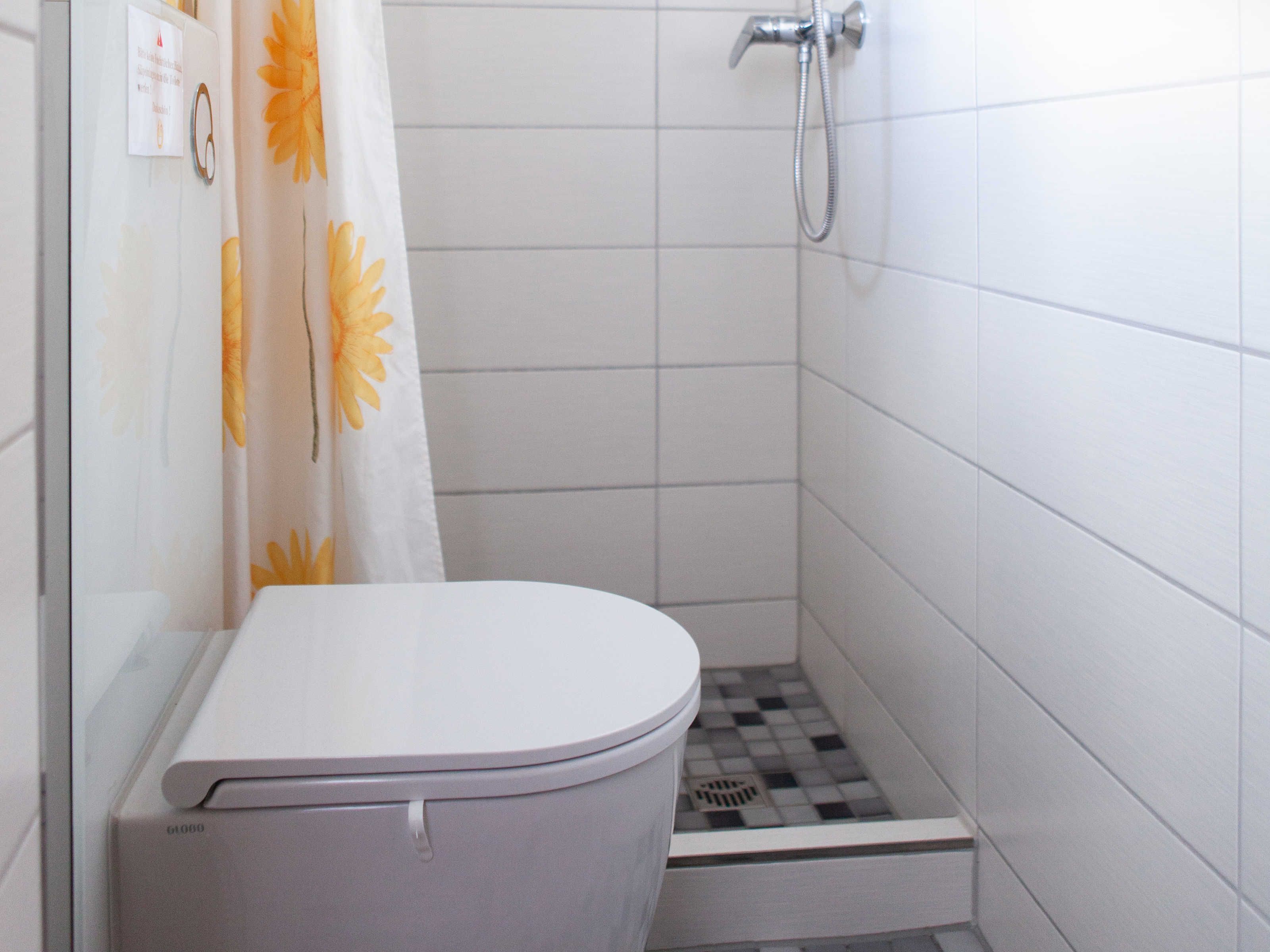 A small, clean bathroom with a toilet, a shower, and a tiled floor.