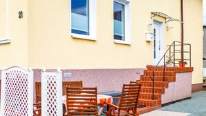 A yellow building with a number 21 sign, a staircase, and outdoor seating with wooden chairs and a table. - Bungalow - Holiday Rentals Liliane (Göhren)