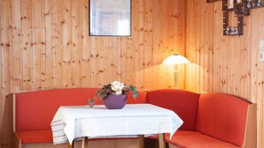 A wooden cabin interior with a red sofa, a small table with a white tablecloth, and a purple vase with flowers. - Bungalow - Holiday Rentals Liliane (Göhren)