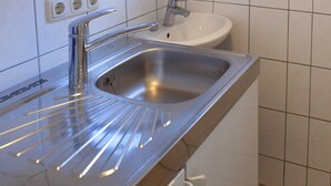 A stainless steel kitchen sink with a faucet, a white countertop, and a white wall with a tiled backsplash. - Bungalow - Holiday Rentals Liliane (Göhren)