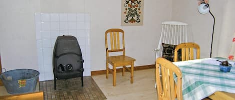 A room with a tiled wall, a wooden chair, a table with a checkered tablecloth, a lamp, and a decorative wall piece.