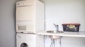 Ein kleiner Waschraum mit Waschmaschine, Trockner und Spüle, neben einer roten Schale.