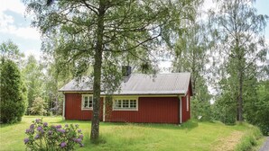 Ein rotes Holzhaus mit geneigtem Dach, umgeben von üppigem Grün und Bäumen.