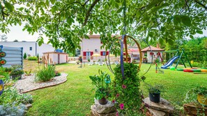 Un jardin bien entretenu, doté d’un espace de jeux comprenant un toboggan et des balançoires, et agrémenté de diverses plantes et fleurs.