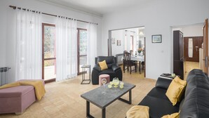 Un salon avec un canapé, une petite table et un fauteuil. Au fond, on aperçoit un coin repas avec une table et des chaises.