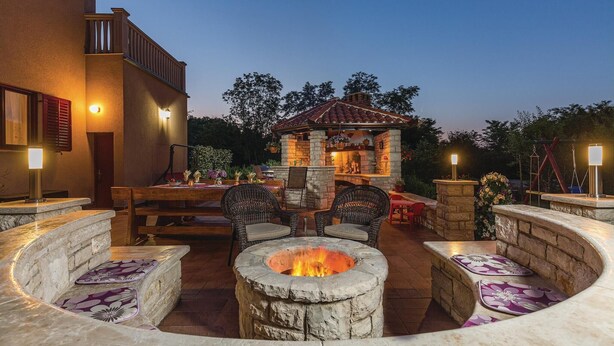 Une terrasse extérieure avec des sièges en pierre, un foyer et un espace barbecue en pierre.