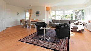 A spacious living area with a dining table, two armchairs, a sofa, and a large window providing natural light.