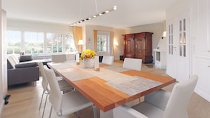 A spacious dining area with a wooden table, white chairs, and a vase of flowers.