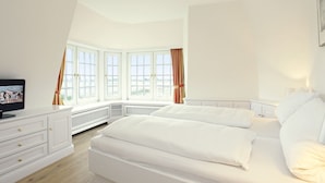 A bedroom with a large bed, a TV on a dresser, and a view of the outdoors through large windows.