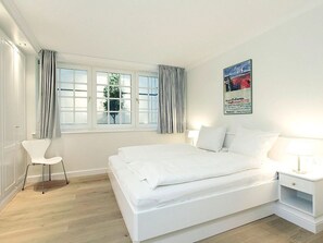 A bedroom with a bed, a chair, a nightstand, and a window with curtains.