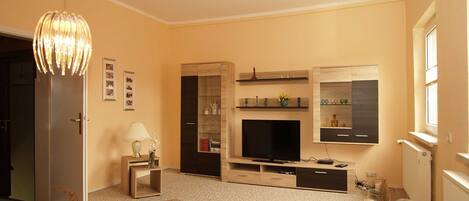 A modern living room with a flat-screen TV, wooden entertainment unit, and a cozy seating area.