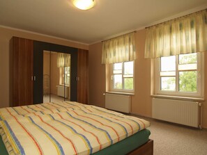 Une chambre à coucher comprenant un lit, une armoire, un miroir et deux fenêtres avec des rideaux.
