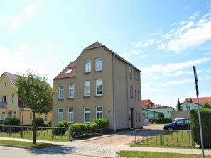 Un immeuble résidentiel à plusieurs étages, doté d’un toit recouvert de tuiles, de nombreuses fenêtres et d’une allée pavée.