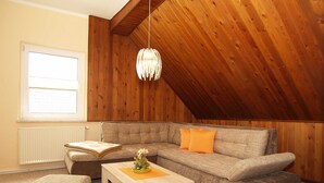 A cozy loft-style living room with a sloped ceiling, a wooden wall, a sofa, a coffee table, and a window with blinds. - KR-07 - Karl-Risch-Str. 7 units. Above. (Kühlungsborn)