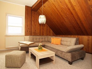 A cozy loft-style living room with a sloped ceiling, a wooden wall, a sofa, a coffee table, and a window with blinds. - KR-07 - Karl-Risch-Str. 7 units. Above. (Kühlungsborn)