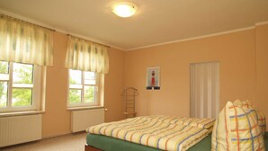A bedroom with a bed, two windows, a radiator, a wall-mounted ladder, and a poster. - KR-07 - Karl-Risch-Str. 7 units. Above. (Kühlungsborn)