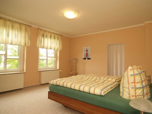 Une chambre à coucher avec un lit, deux fenêtres, un radiateur, une échelle fixée au mur et une affiche.