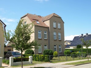 Un immeuble résidentiel à plusieurs étages, doté d’un toit recouvert de tuiles, de nombreuses fenêtres et d’une allée pavée.