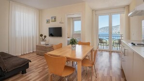 A compact living space with a dining area, a sofa, a TV, and a balcony with a view. - Kis Residence (Korcula)