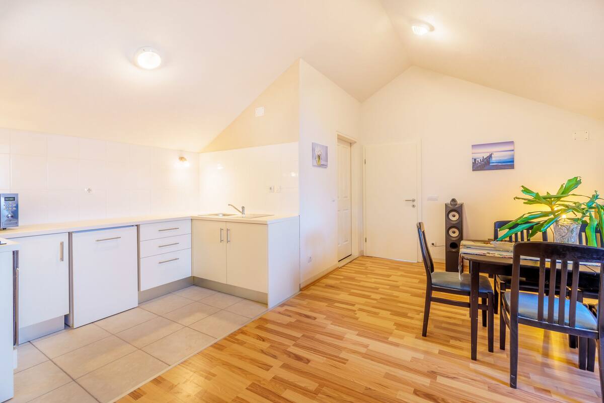 A modern kitchen with white cabinets, a wooden dining table with chairs, and a potted plant.
