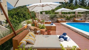 A wooden deck with outdoor seating, a pool, and umbrellas. - Kis Residence (Korcula)
