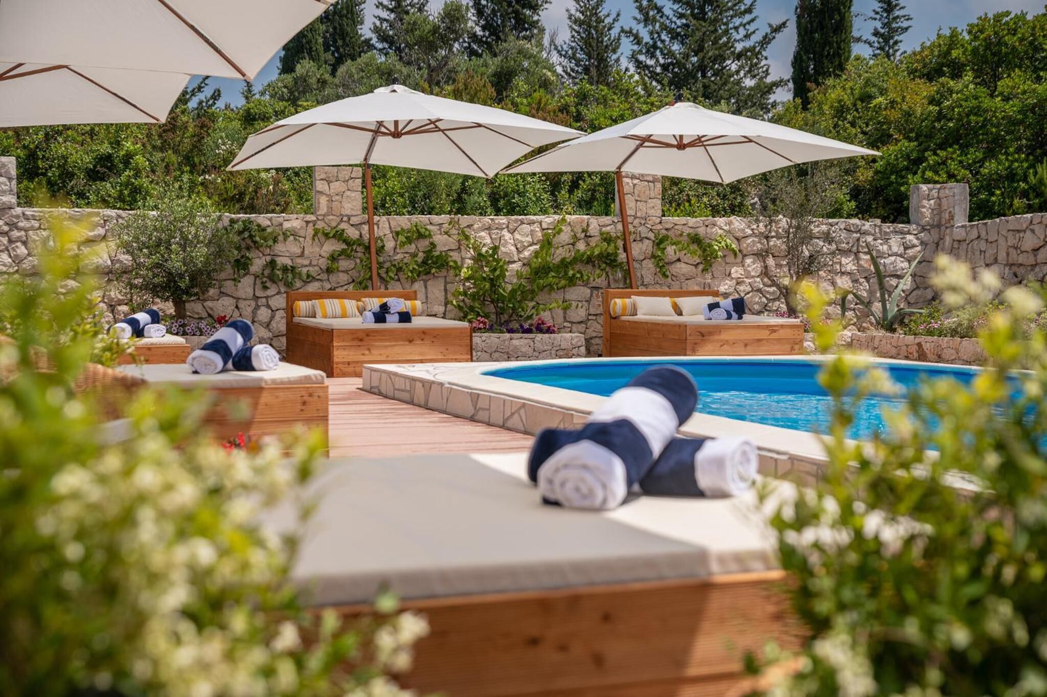 A poolside area with wooden loungers, umbrellas, and a stone wall.