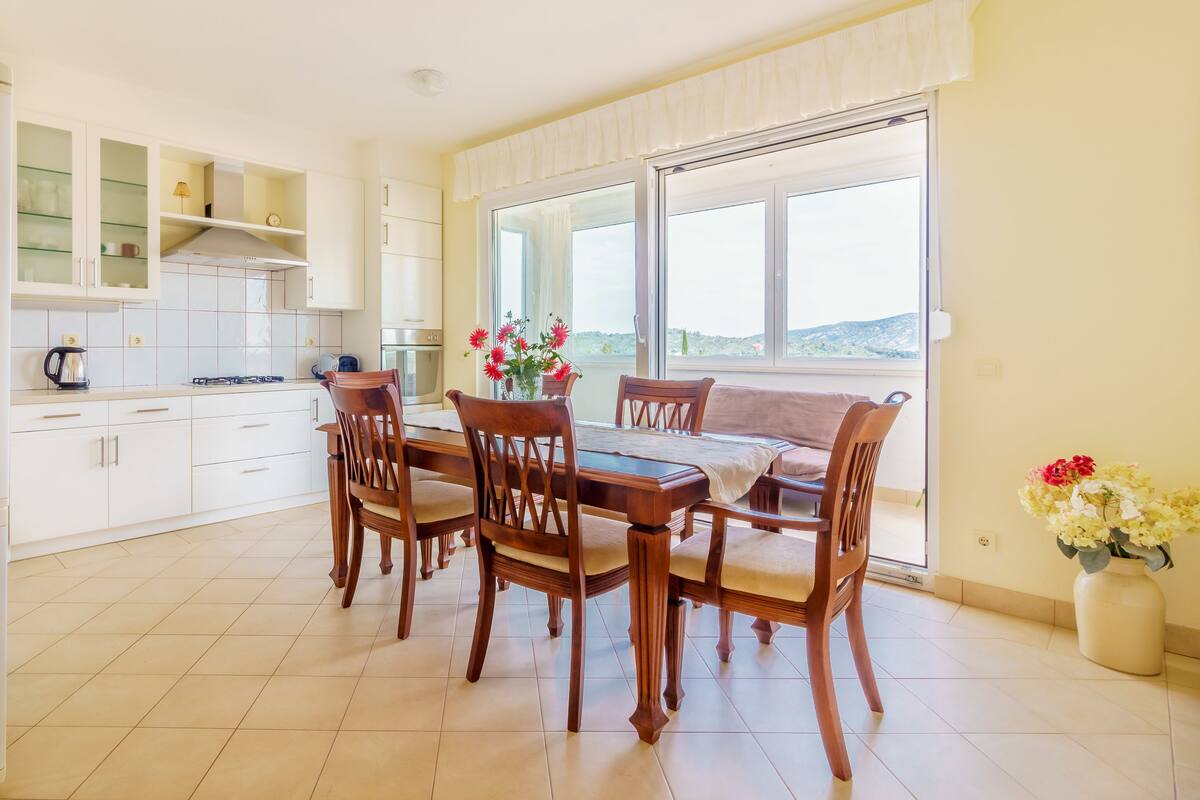 A modern kitchen with white cabinets, a dining table with chairs, and a large window offering a view of the outdoors.