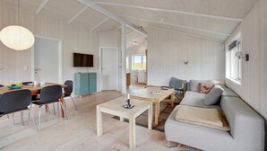 A spacious living area with a wooden floor, a sofa, a dining table with chairs, and a television mounted on the wall. - Awesome home in Askeby with sauna (Askeby)