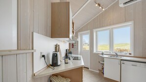 A modern kitchen with wooden cabinets, a built-in oven, a sink, and a window with a view of the countryside. - Awesome home in Askeby with sauna (Askeby)
