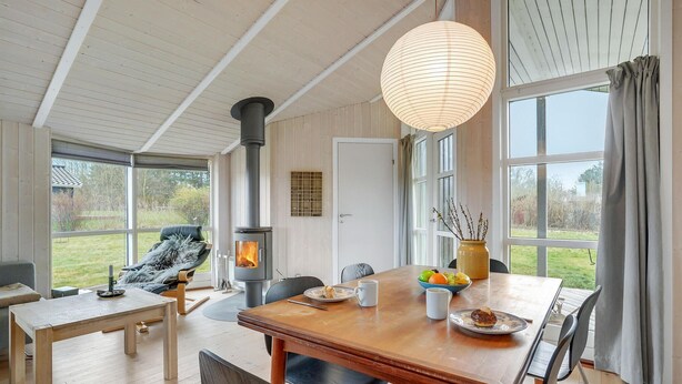 A cozy room with a wooden table, chairs, a sofa, a large window, and a wood-burning stove. - Awesome home in Askeby with sauna (Askeby)