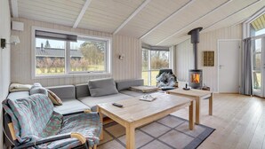A cozy room with a wooden ceiling, a large window, a sofa, a chair, a table, and a wood-burning stove. - Awesome home in Askeby with sauna (Askeby)