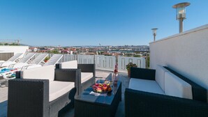 Une terrasse sur le toit, avec des chaises longues, une table garnie de fruits et de boissons, et une vue sur la ville.