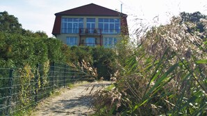 Ein zweistöckiges Haus mit rotem Dach, umgeben von dichter Vegetation und einem Metallzaun.