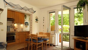 Eine kompakte Küche mit Holzschränken, einem Esstisch mit Stühlen, einem Fernseher und einem großen Fenster mit Blick auf Grünflächen.