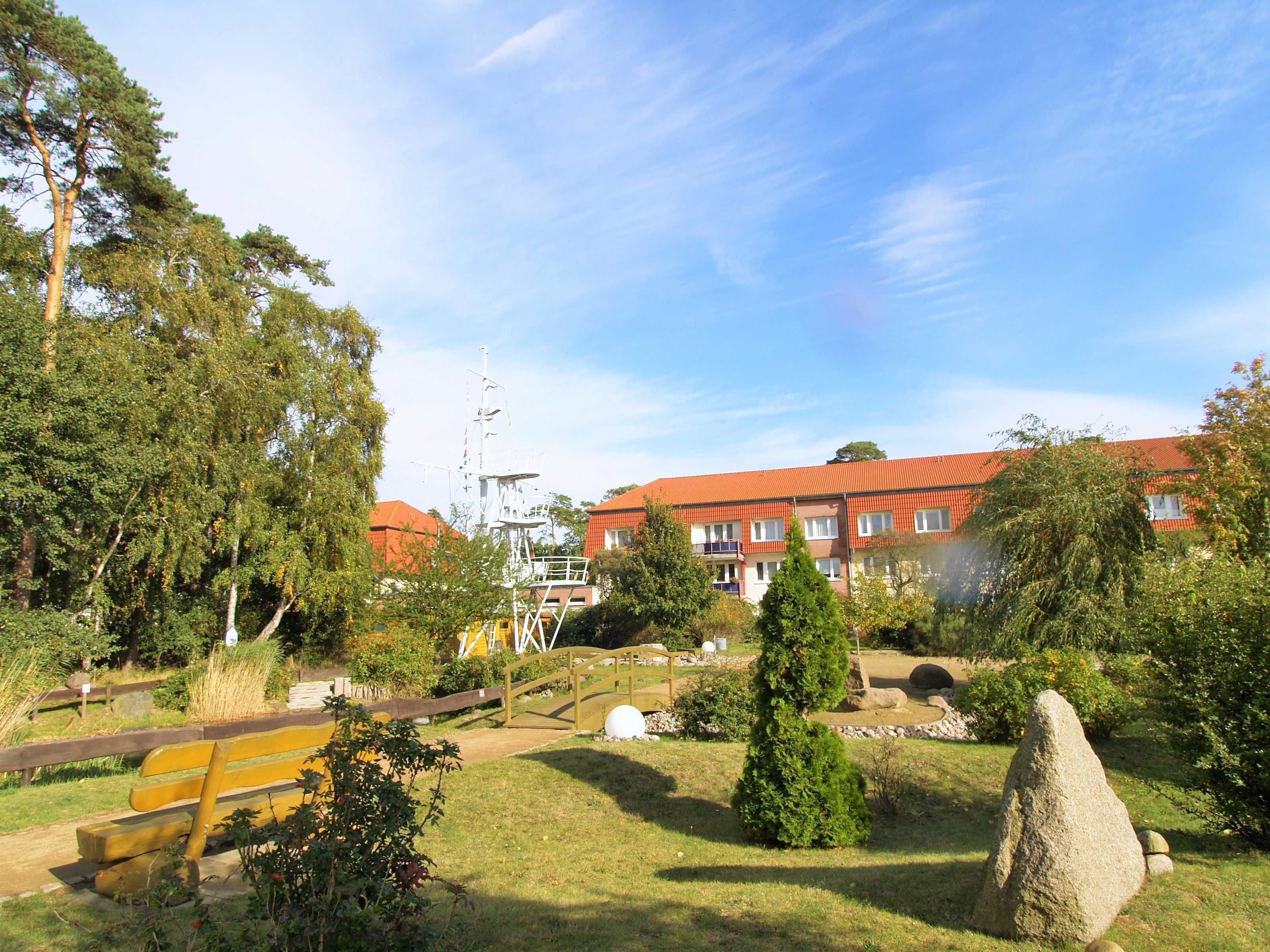 Zona residencial con un edificio de techo rojo, un puente de madera y un parque cubierto de césped con un monumento de piedra.