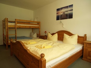Une chambre avec un lit simple en bois, un lit superposé, une table de chevet et une lampe fixée au mur.
